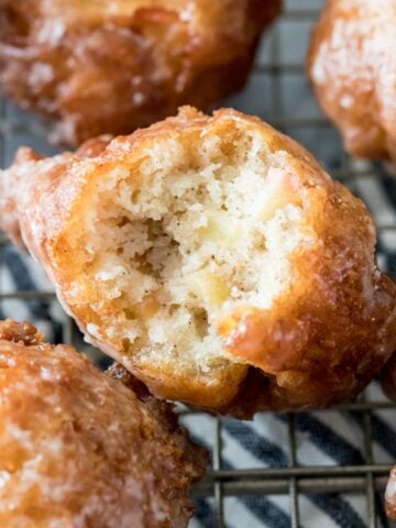 glazed apple fritters on a cooling rack with the center fritter missing one bite