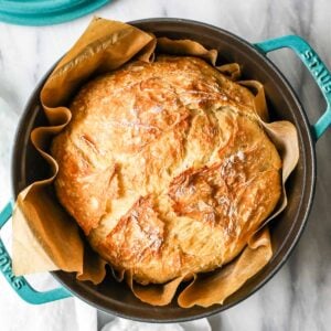 Overhead view of a round loaf of artisan bread in a teal dutch oven.