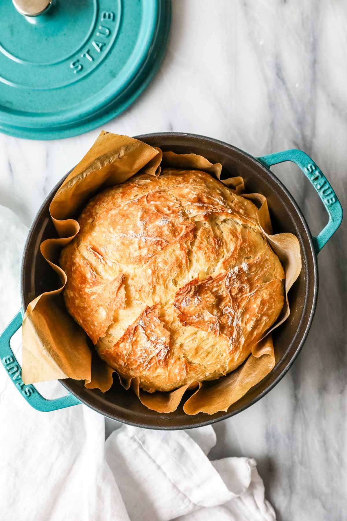 Overhead view of a round loaf of artisan bread in a teal dutch oven.