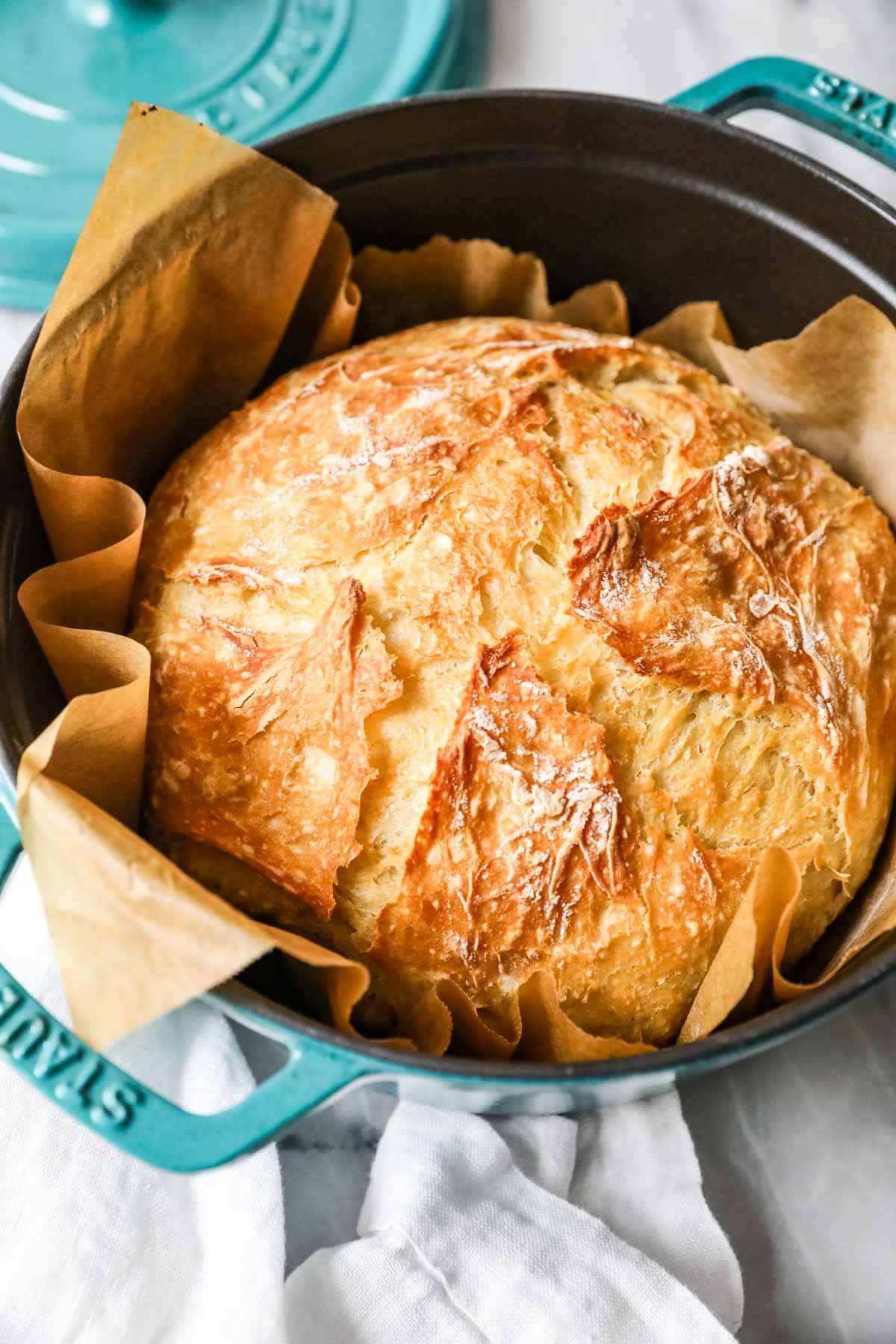 Loaf of homemade crusty artisan bread in a teal dutch oven.