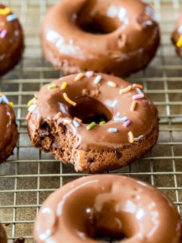 Chocolate donuts topped with chocolate glaze and sprinkles on a cooling rack.