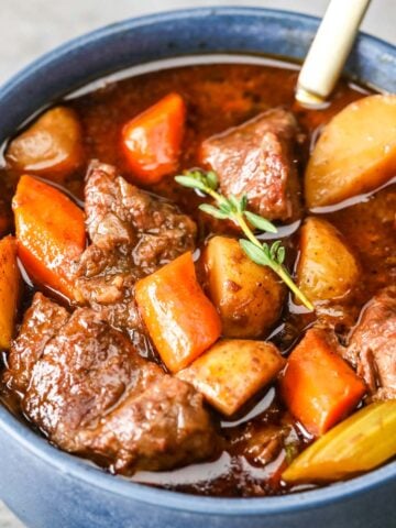 Blue bowl of beef stew with chunks of beef, carrots, and potatoes.