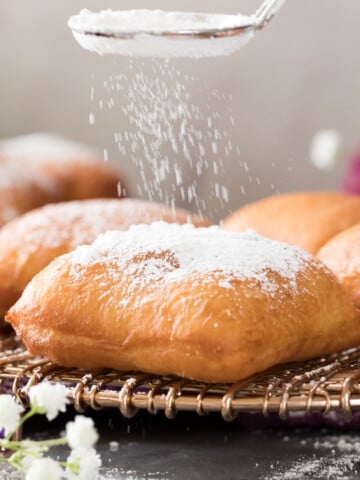 sprinkling powdered sugar over golden brown beignet