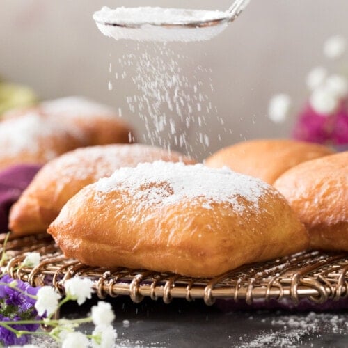 sprinkling powdered sugar over golden brown beignet