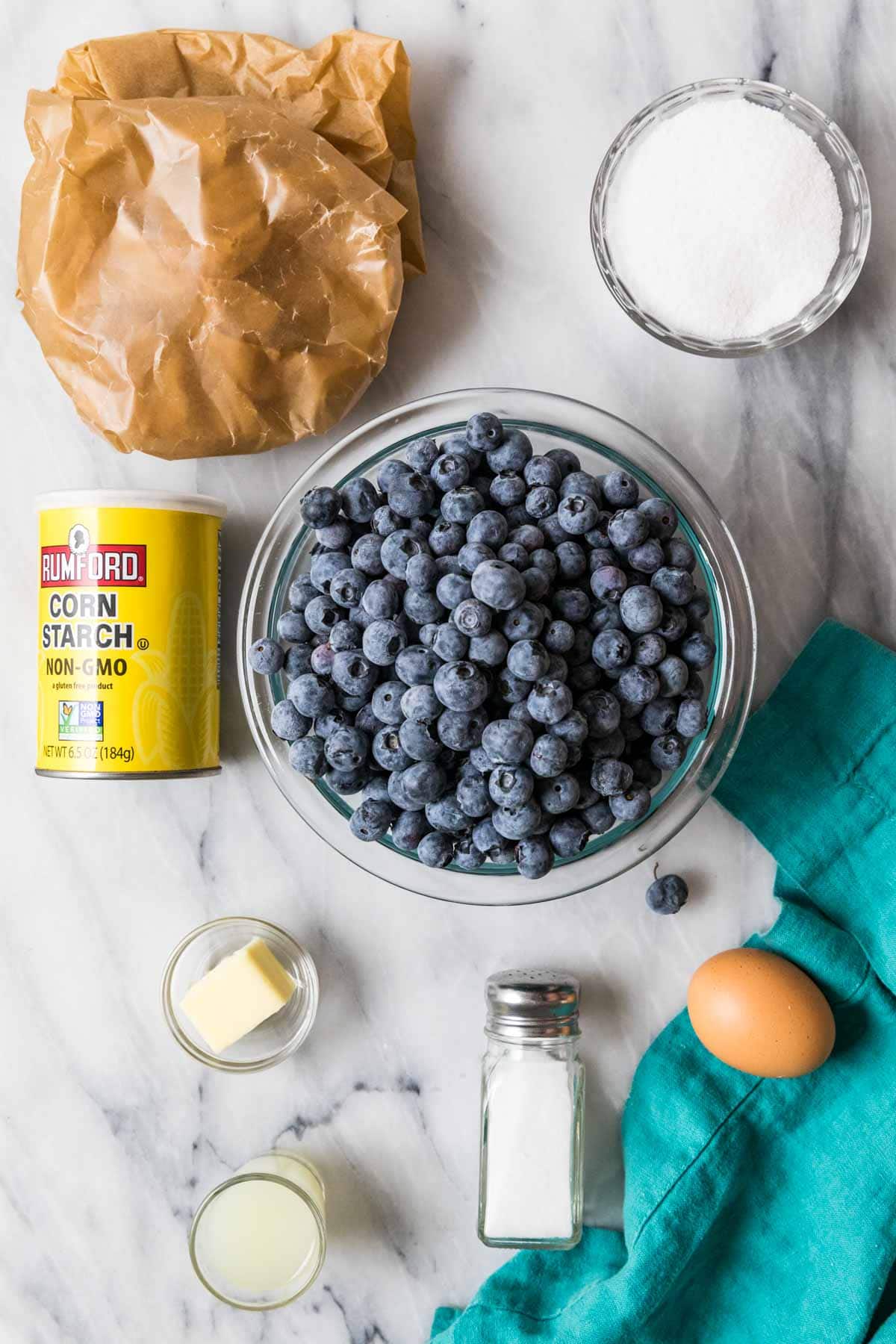 Overhead view of ingredients including blueberries, pie crust, lemon juice, cornstarch, and more.