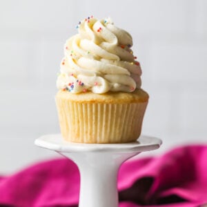 Vanilla cupcake on a pedestal topped with a tall swirl of vanilla bean frosting.