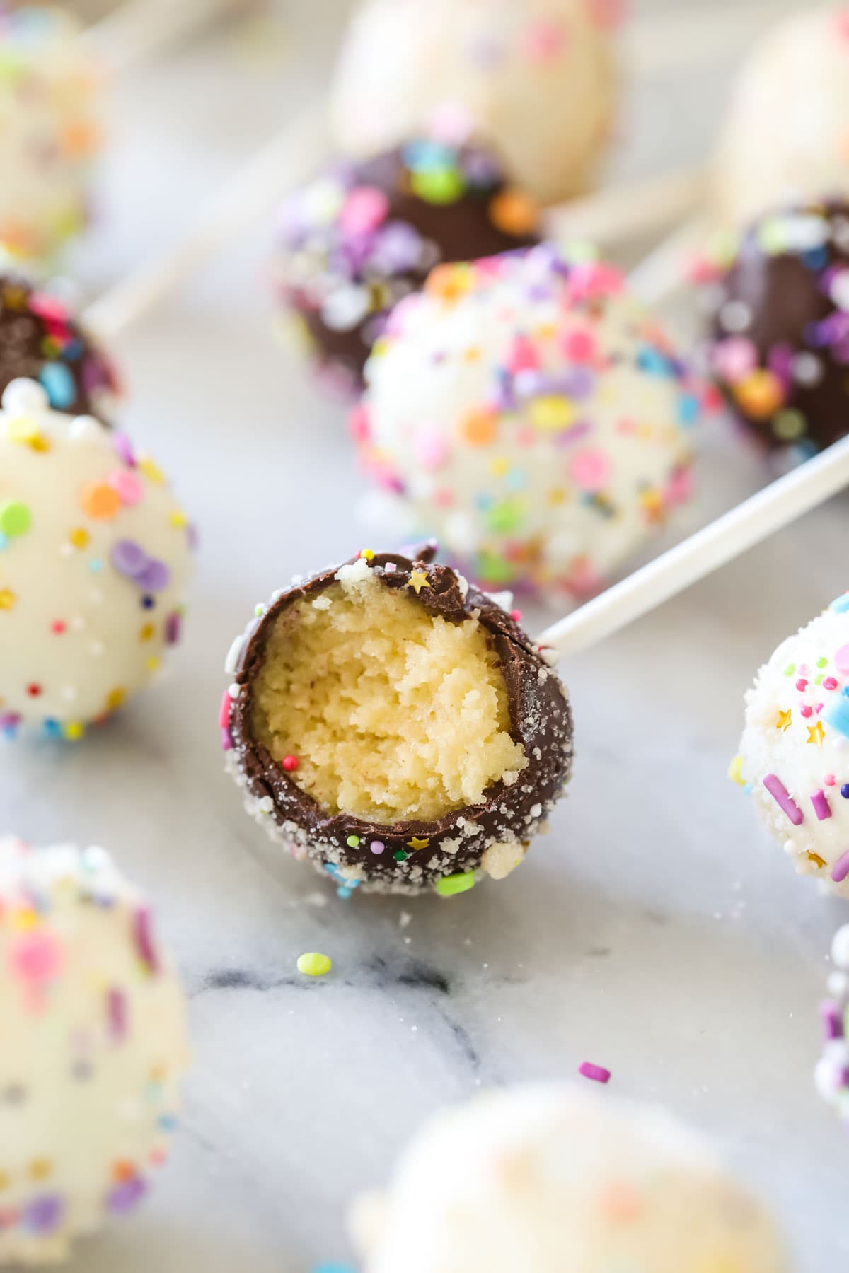 Chocolate covered cake pop bitten to show a yellow cake filling surrounded by other cake pops.