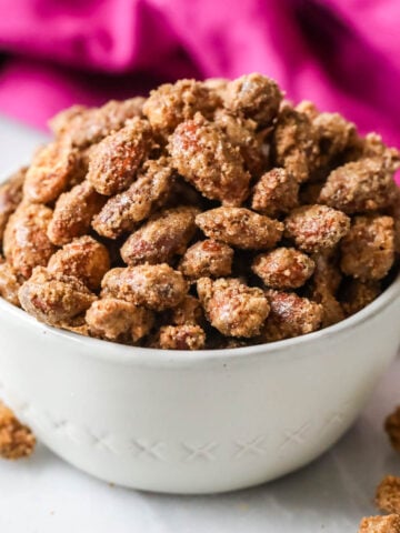 White bowl of candied almonds with a bright pink tea towel in the background.