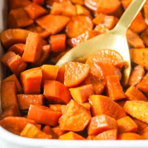 Casserole dish of candied yams with a gold spoon scooping a serving.