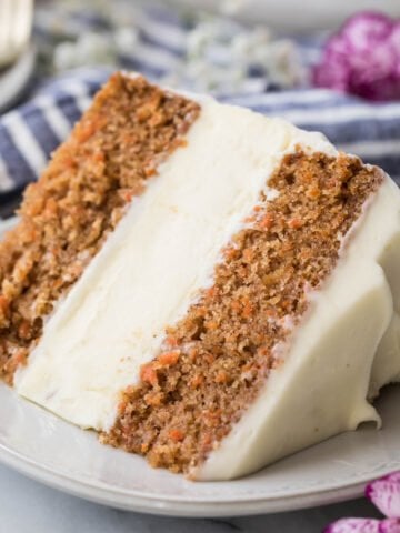 slice of carrot cake cheesecake frosted with cream cheese icing on a white plate