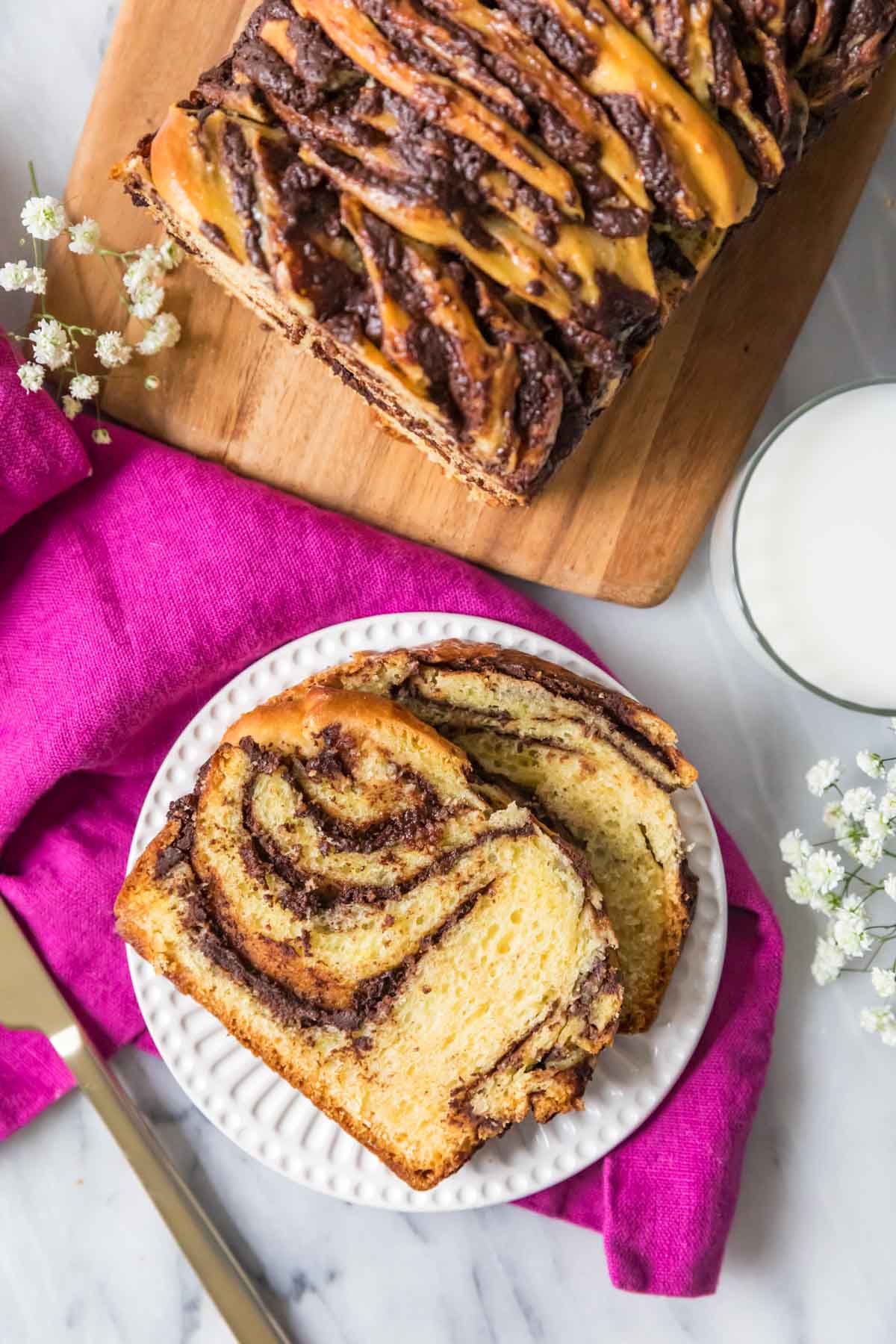 Overhead view of sliced of swirled chocolate bread on a plate with the remaining loaf beside it.