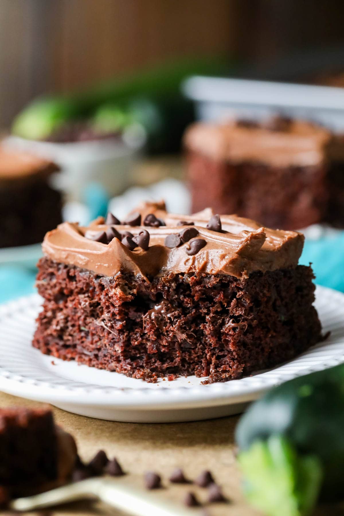 Square slice of frosted chocolate zucchini cake missing a bite.