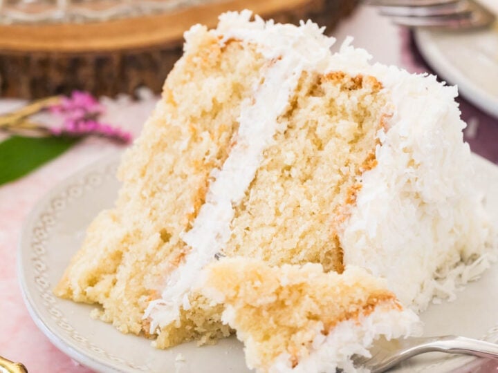 Slice of coconut cake on a plate with a forkful missing