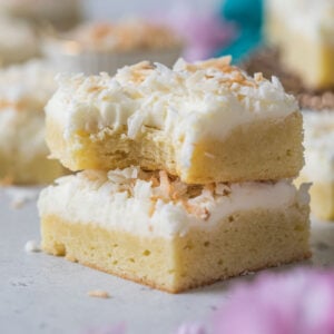 Two coconut cream bars stacked on top of each other, with the top bar missing a bite.