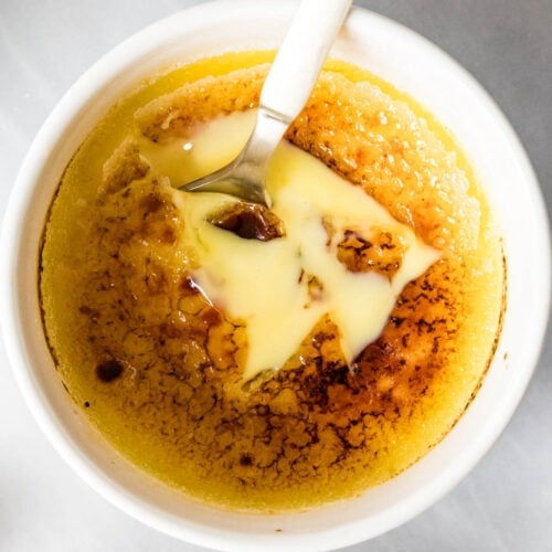 Overhead of creme brulee in a ramekin - golden spoon broke through surface to show custard beneath