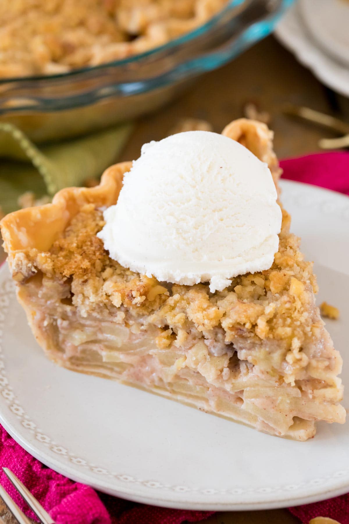 Slice of Dutch apple pie topped with a scoop of vanilla ice cream on a white plate.