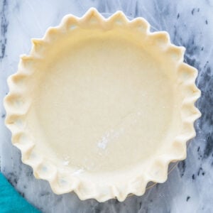 Overhead view of unbaked homemade pie crust with fluted edge on gray marble countertop