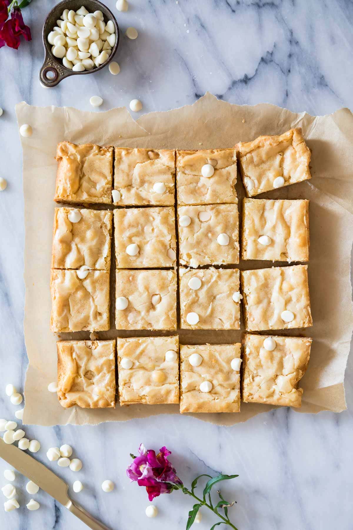 Overhead view of a batch of white chocolate brownies cut into 16 pieces.