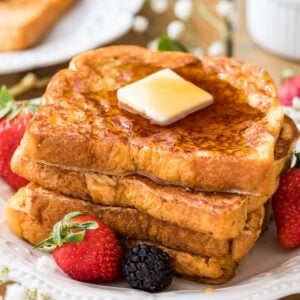 Stack of french toast with butter on top and berries scattered around.