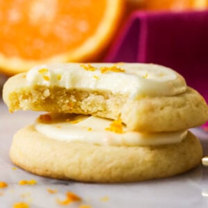 Two orange cookies stacked on top of each other with the top cookie missing one bite.