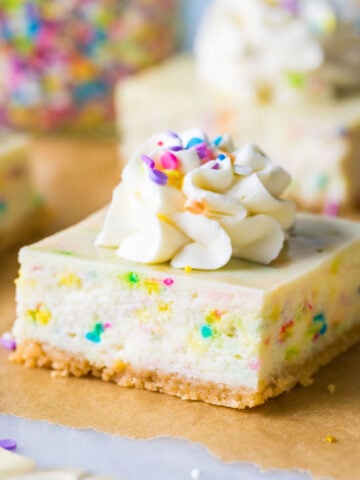 funfetti cheesecake bar topped with whipped cream and sprinkles on brown parchment