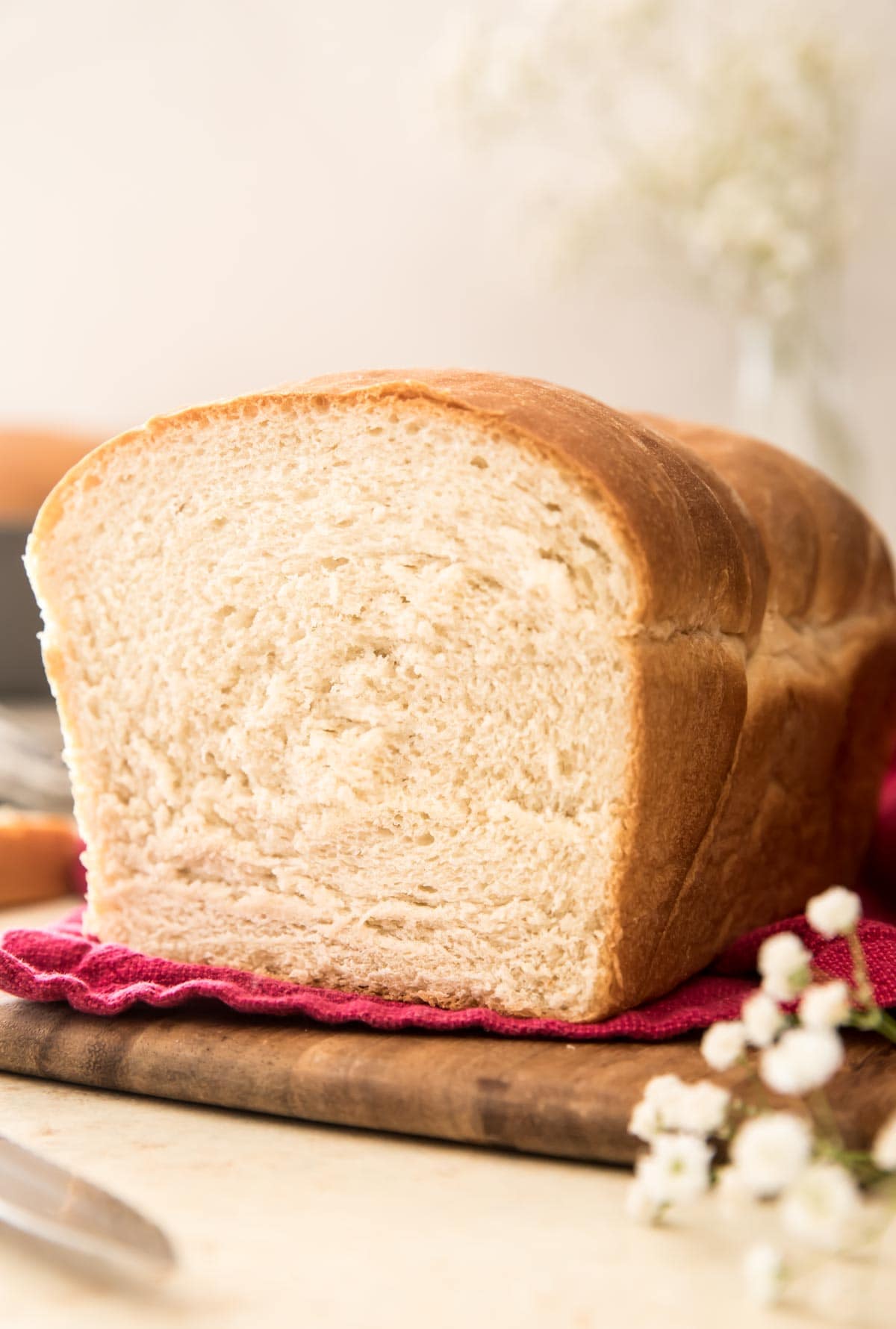 loaf of bread on a red towel on a wooden cutting board with white flowers in foreground and background