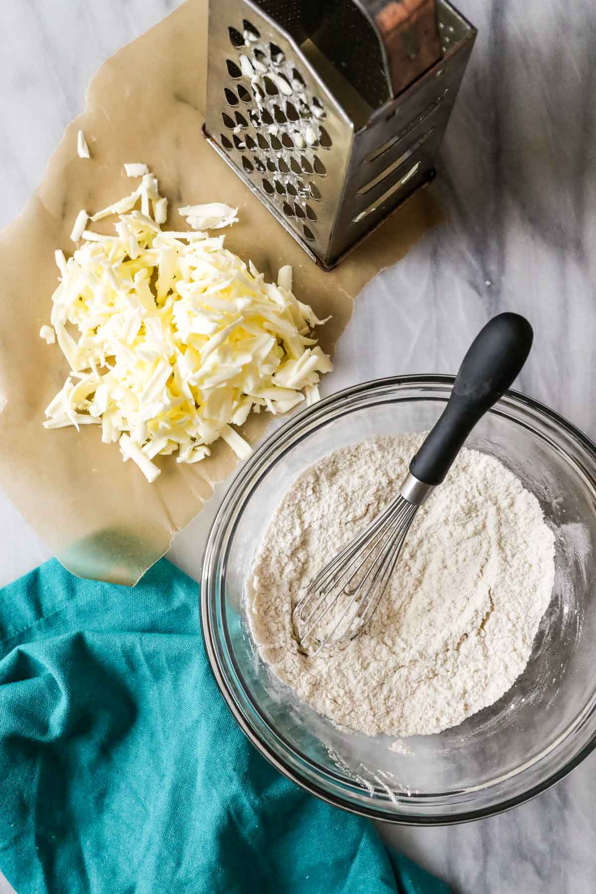 Overhead view of grated butter and a bowl of whisked dry ingredients.