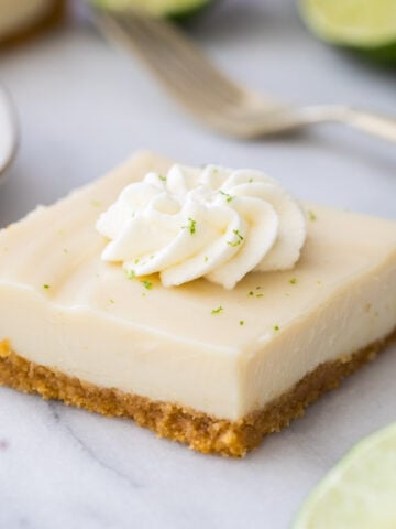 square of creamy key lime pie bar on marble, topped with whipped cream and lime zest