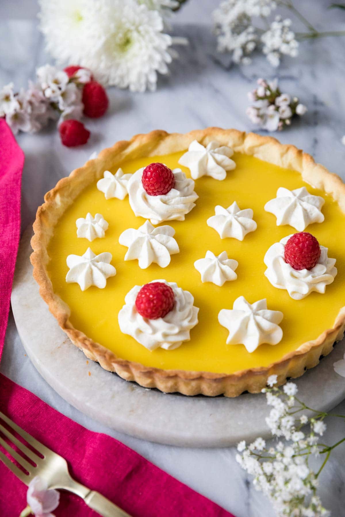 Lemon tart decorated with piped whipped cream and raspberries.