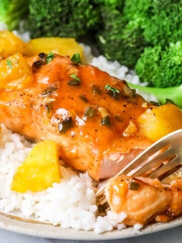 Fork cutting into maple glazed salmon served on a bed of rice with a side of broccoli.