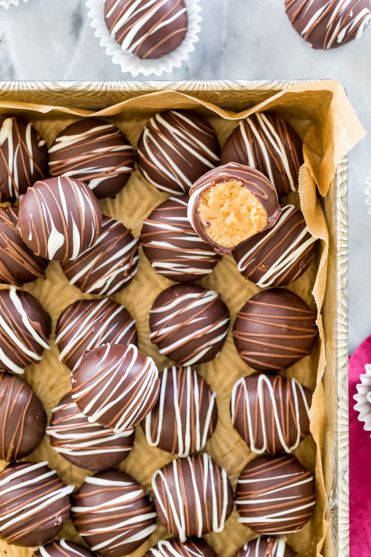 top down view of chocolate coated peanut butter balls decorated with white and milk chocolate in parchment lined metal serving dish