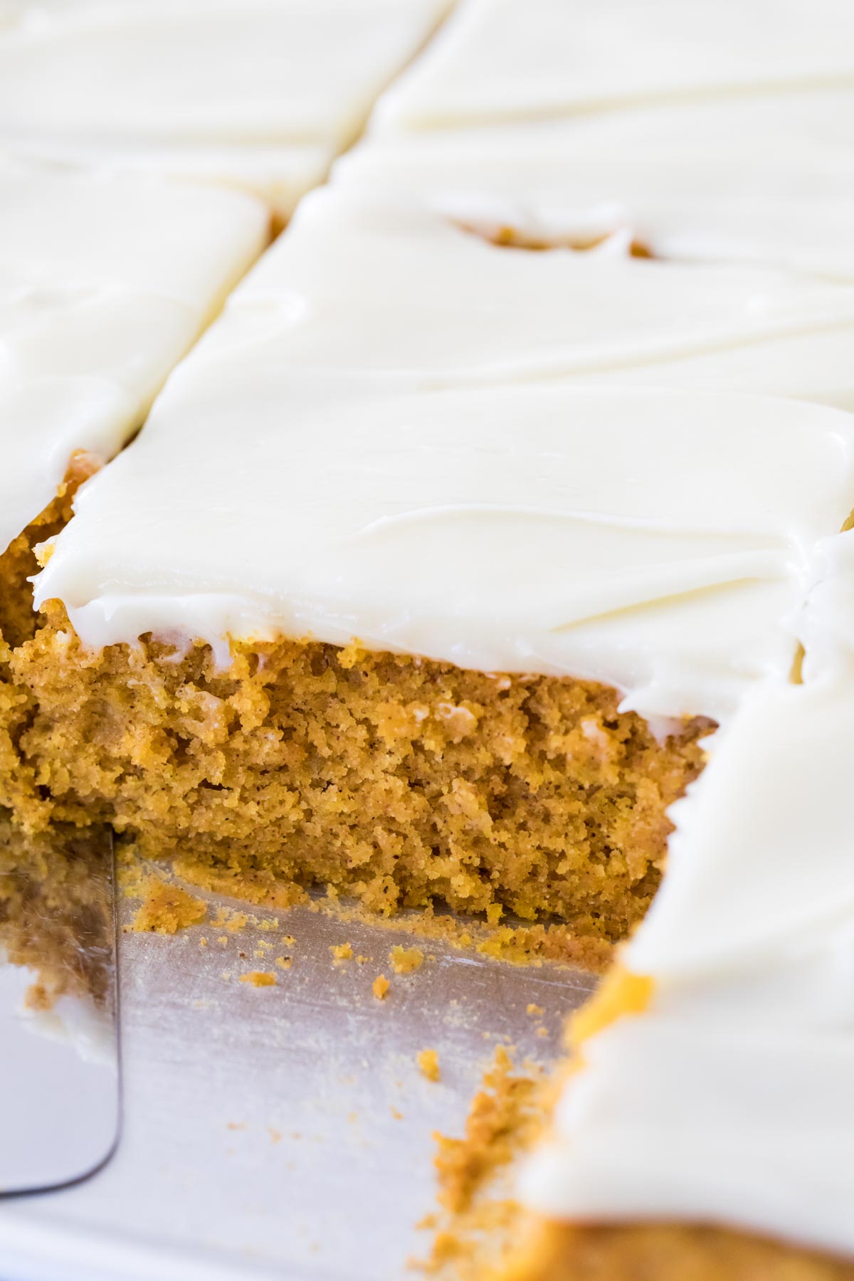 Close-up view of a metal pan of bars frosted with cream cheese frosting just after being cut.