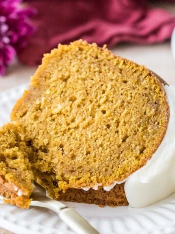 Slice of pumpkin bundt cake topped with cream cheese glaze on a plate with a fork taking one bite.