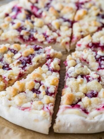 Close-up view of a raspberry cheesecake dessert pizza topped with white chocolate chips and streusel.