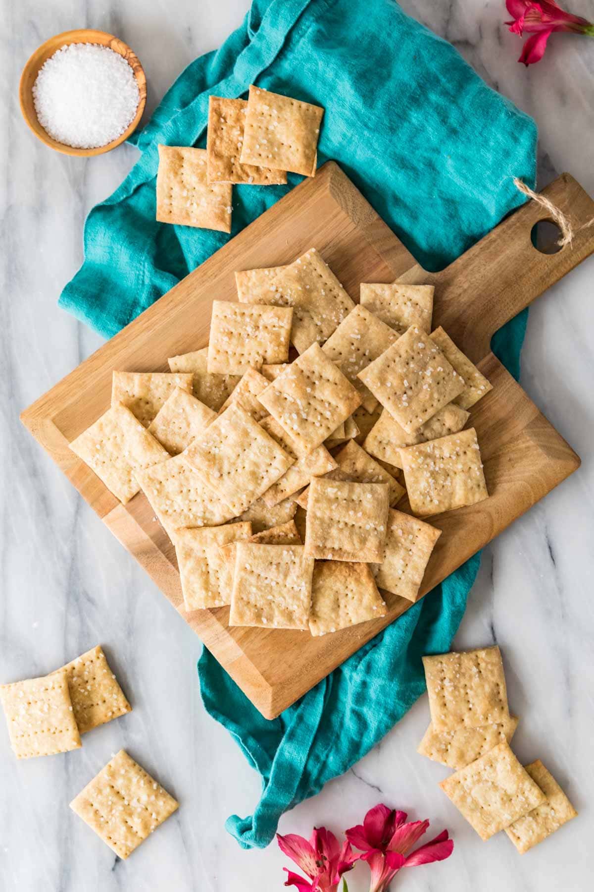 Overhead view of sourdough crackers scattered across a wooden cutting board.