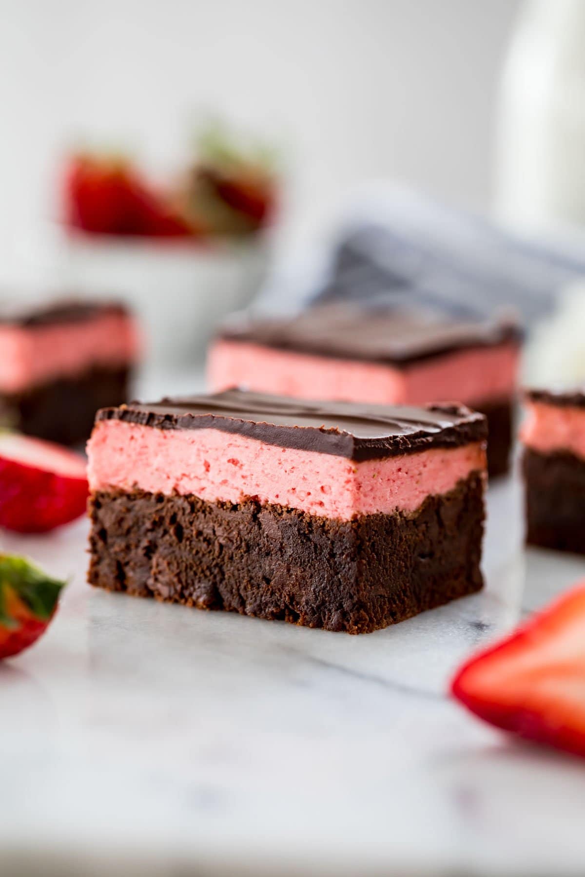 close-up view of a strawberry brownie consisting of a brownie layer, strawberry icing layer, and a final layer of chocolate ganache