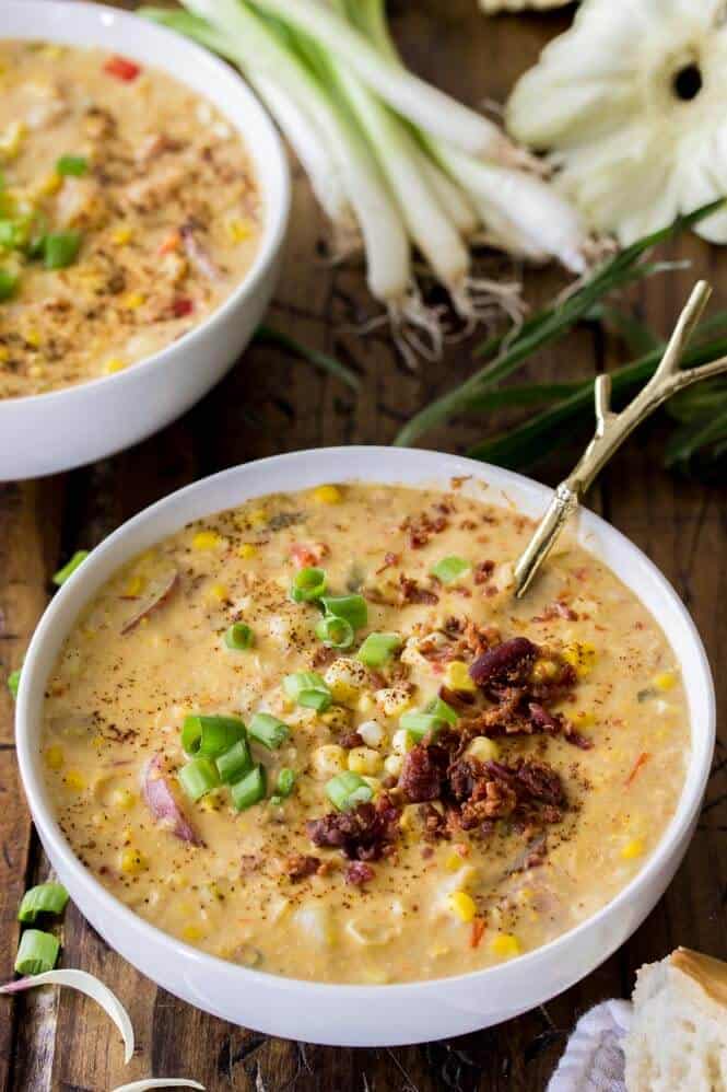 Corn chowder in white bowl, topped with bacon and chives