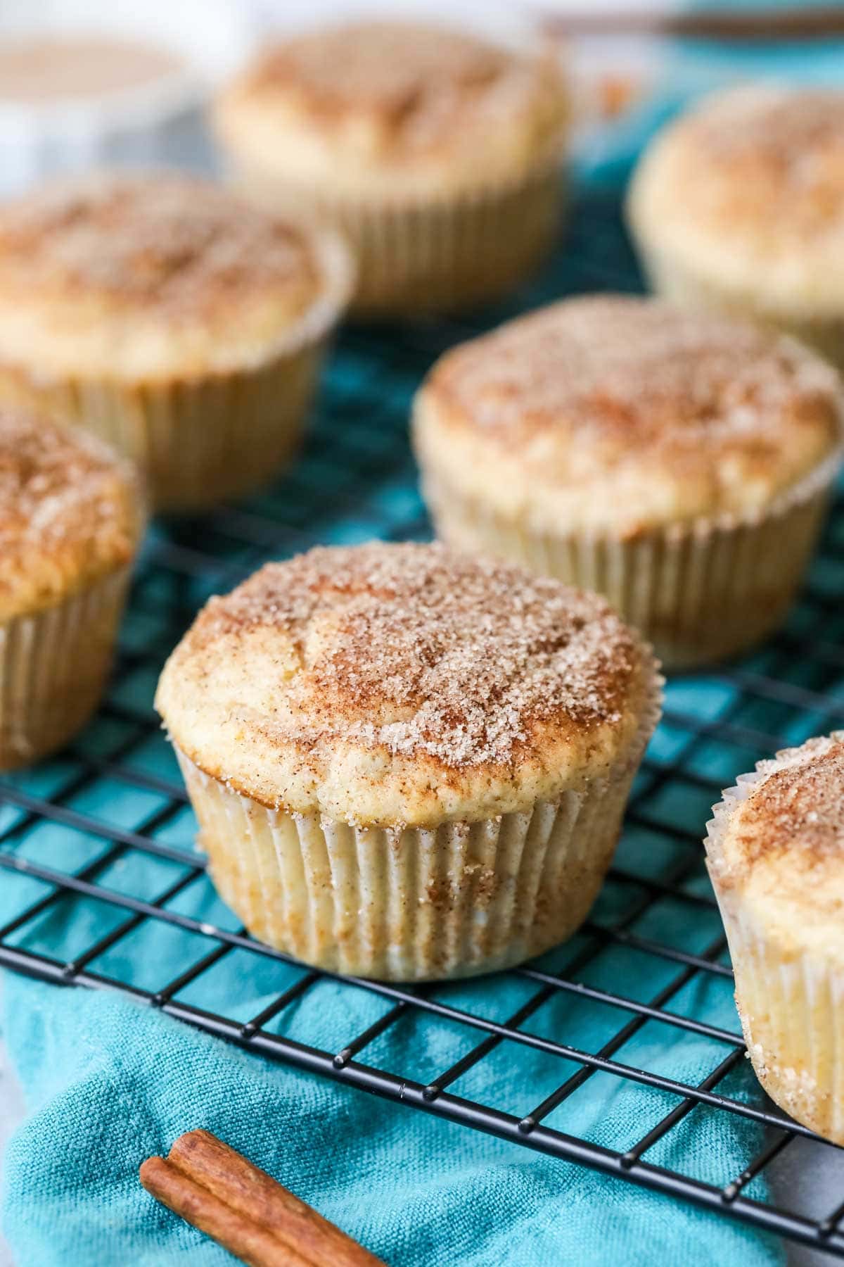 Cinnamon muffins on a cooling rack with a teal towel underneath.