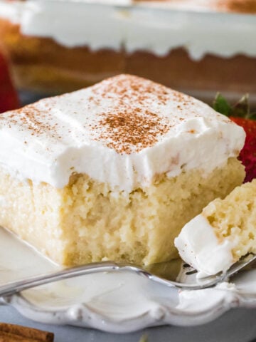 square slice of tres leches cake with one forkful sitting on the plate beside it