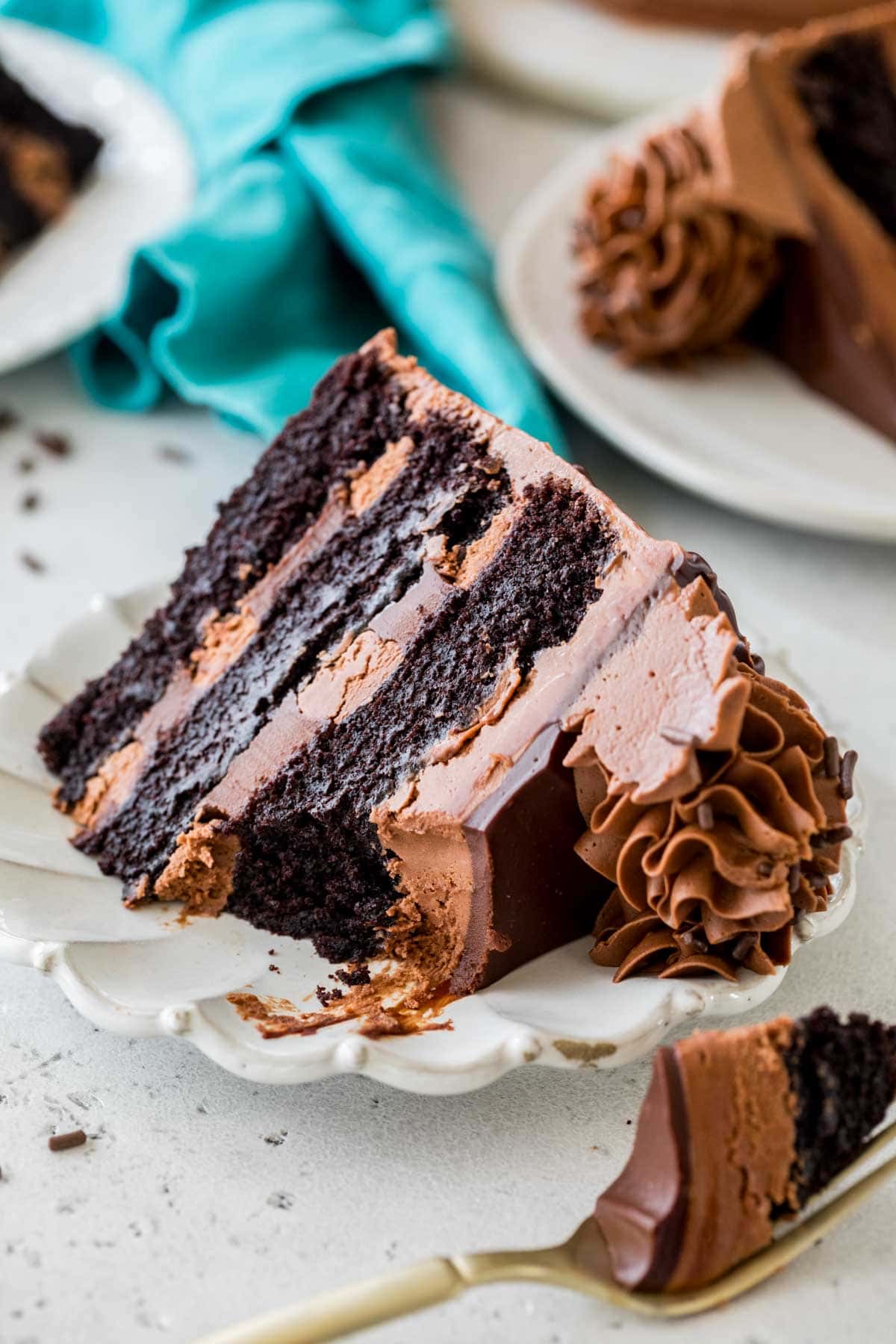 Slice of triple chocolate cake missing a bite on a white plate.